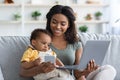 Woman working with laptop and cellphone at home with child in arms Royalty Free Stock Photo