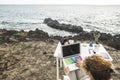 Woman working on laptop with colorful keyboard while sitting at the sea coast with her feet resting on table desk in front of