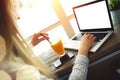 Woman working at a laptop in the comfortable trendy cafe sitting near a large window at a table with a glass of or Royalty Free Stock Photo