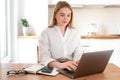 Woman working on laptop at home on kitchen. talking on phone. Blonde woman business. Woman trying to find a job