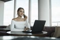 Woman working on laptop at office while talking on phone, backlit warm light. Portrait of young smiling business woman Royalty Free Stock Photo