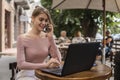 Woman working on laptop at office while talking on phone, backlit warm light. Portrait of young smiling business woman Royalty Free Stock Photo