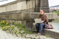 Woman working on laptop while sitting near the river promenade in the old town. Royalty Free Stock Photo