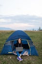 Woman working on laptop in tent in nature. Young freelancer sitting in camp. Relaxing in camping site in mountains Royalty Free Stock Photo