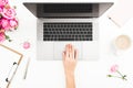 Woman working on laptop. Workspace with female hands, laptop, pink roses bouquet, coffee mug, diary on white table. Top view. Flat