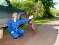 The woman in working overalls tries to replace a wheel at an off-road car, and asks the help Royalty Free Stock Photo