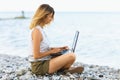 A woman works at a computer on the seashore, combines rest and work