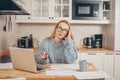 A woman works from home using a laptop. A beautiful blonde in a sweater and glasses, there is a mug and papers on the table. Home Royalty Free Stock Photo