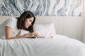 Woman works with laptop on the bed in concept of workation. Royalty Free Stock Photo