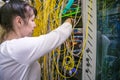 The woman works in the server room of the data center. The girl switches fiber-optic Internet wires in a rack with powerful