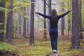 Woman worshiping with open arms in an autumn misty forest with yellow, green and red leaves