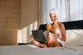 Woman wrapped in a bath towel lying in bed with a laptop on her lap and holding a smartphone in her hands. Lifestyle Royalty Free Stock Photo
