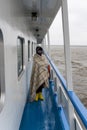 woman wrapped in a plaid walks along the side of a ship sailing on sea