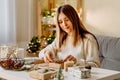 Woman wrapping Christmas eco natural gift boxes at home. Preparing presents on white table with decor elements, lights Royalty Free Stock Photo