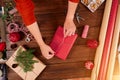 Woman wrapping gift box with decorating items on wood table, close up, top view.