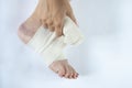 Woman is wrapping her leg with sprained ankle with elastic bandage  on white background. Twisted bandaged ankle with bruis Royalty Free Stock Photo