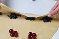 A woman wraps cherries and blueberries in a dough that are lying on a rolled dough. Cooking dumplings
