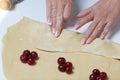 A woman wraps cherries and blueberries in a dough that are lying on a rolled dough. Cooking dumplings