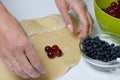 A woman wraps cherries and blueberries in a dough that are lying on a rolled dough. Cooking dumplings