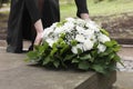 Woman with wreath of flowers near tombstone outdoors, closeup. Funeral attribute Royalty Free Stock Photo