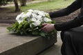 Woman with wreath of flowers near tombstone outdoors, closeup. Funeral attribute Royalty Free Stock Photo