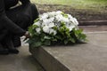 Woman with wreath of flowers near tombstone outdoors, closeup. Funeral attribute Royalty Free Stock Photo