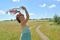 The woman with a wreath on the head holds a colorful scarf in the raised hands against the background of the blossoming buckwheat