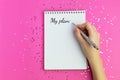 Woman writes plans for New Year. Wish list for Christmas, mockup for your design. Pink background, flat lay style. Silver sparkles Royalty Free Stock Photo