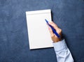 woman writes in notebook on dark blue table, hand in shirt holding a pencil, sketchbook drawing, top view