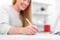 A woman writes while sitting at a table in an office or classroom. The girl fills the documents at the workplace using a