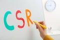 Woman writing abbreviation CSR on magnetic whiteboard closeup. Corporate social responsibility