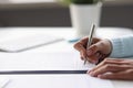 Woman writing with ballpoint pen in documents at table at home closeup