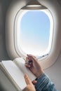 Woman writing on blank notebook while travelling on plane. Royalty Free Stock Photo