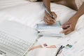 Woman Writing cheque on bed by laptop