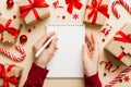 Woman writing Christmas to do list on notebook on colored background with xmas decorations