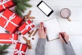 Woman writing New year goals (to do list) to notebook on desk with Christmas decorations.