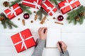 Woman writing New year goals & x28;or to do list& x29; to notebook on white desk with red gift boxes, fir tree branches. Royalty Free Stock Photo