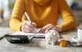 A woman is writing in a notebook with a piggy bank on the table by AI generated image Royalty Free Stock Photo