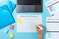 Woman writing at planner on blue pastel background with laptop and stationery Royalty Free Stock Photo