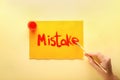 Woman writing word MISTAKE with paint on sheet of paper against color background