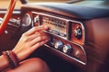 A woman& x27;s hand adjusting the controls of an antique car radio. Radio is vintage style, with metal buttons and dials.