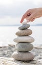 Woman& x27;s hand balancing a stack of stones on a driftwood beach log.