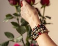 A woman& x27;s hand with bracelets made of jasper, obsidian and tiger& x27;s eye stones touches a bouquet of roses Royalty Free Stock Photo