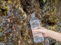 A woman& x27;s hand fills a plastic bottle with spring water from a spring flowing down a rock.