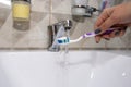 A woman& x27;s hand holding a toothbrush and toothpaste under running water from the tap. Royalty Free Stock Photo