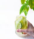 A woman& x27;s hand holds glass mug with handle with refreshing detox lemonade with sliced lime, lemon, cucumbers and red Royalty Free Stock Photo