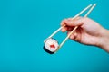 Woman& x27;s hand holds tasty sushi roll maki with wooden chopsticks on blue background. Place for caption and text Royalty Free Stock Photo