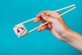 Woman& x27;s hand holds tasty sushi roll maki with wooden chopsticks on blue background. Place for caption and text Royalty Free Stock Photo