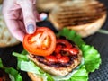 A woman's hand lays down a slice of tomato on a delicious homemade burger. Handmade homemade burgers, close-up