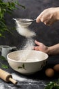Woman& x27;s hand sifting flour through sieve. Selective focus. Baking, cooking, pastry abstract concept. Dark background